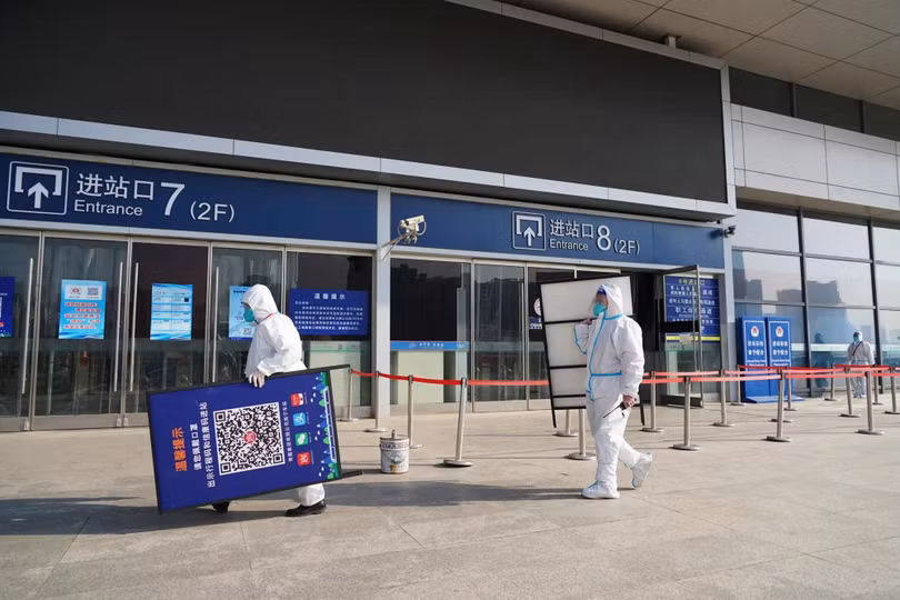 Công nhân trong bộ đồ bảo hộ tháo bỏ các dấu hiệu mã y tế sau khi chính phủ rút lại các biện pháp kiểm soát đại dịch tại lối vào một nhà ga đường sắt ở Tây Ninh, tỉnh Thanh Hải. Ảnh: Reuters