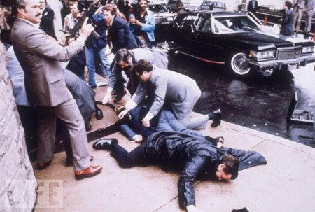 Vào ngày 30/3/1981, John Hickley Jr. bắn 6 phát đạn nhằm vào TT Ronald Reagan khi ông rời khách sạn Hilton ở Washington D.C. Trong ảnh, Mật vụ bao quanh tổng thống và những người đi cùng đoàn với ông. Tổng thống bị dính một phát đạn còn đại diện báo chí của ông bị thương nặng.