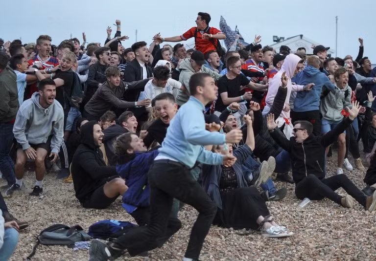 Nhóm cổ động viên tập trung tại bãi biển Brighton để theo dõi trận đấu qua màn hình lớn. Ảnh: Metro