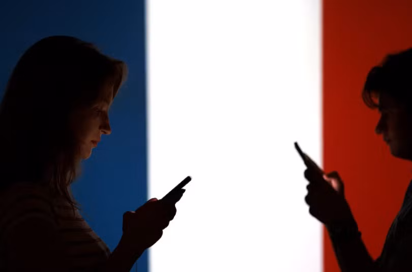 Bức ảnh minh họa cho thấy các thiếu niên tạo dáng chụp ảnh với điện thoại thông minh trên tay trước lá cờ Pháp. Ảnh: Reuters.