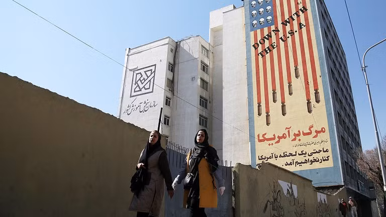 Hai phụ nữ đi qua một biểu ngữ nội dung chống Mỹ ở Tehran, Iran. Ảnh: Getty.