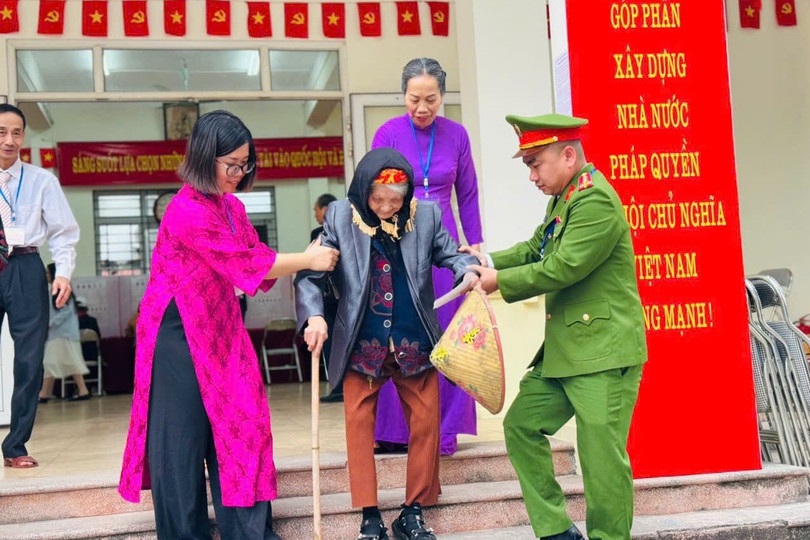 Cử tri cao tuổi được cán bộ tổ bầu cử hỗ trợ di chuyển ở điểm bầu cử tại Hà Nội hôm 15/3.