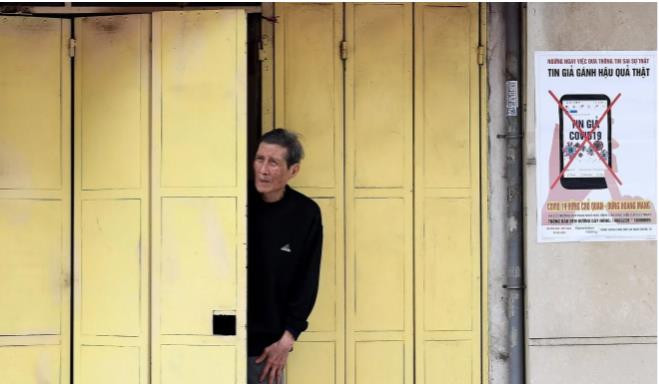 Một người đàn ông đứng cạnh tấm áp phích kêu gọi cộng đồng không lan truyền tin tức giả