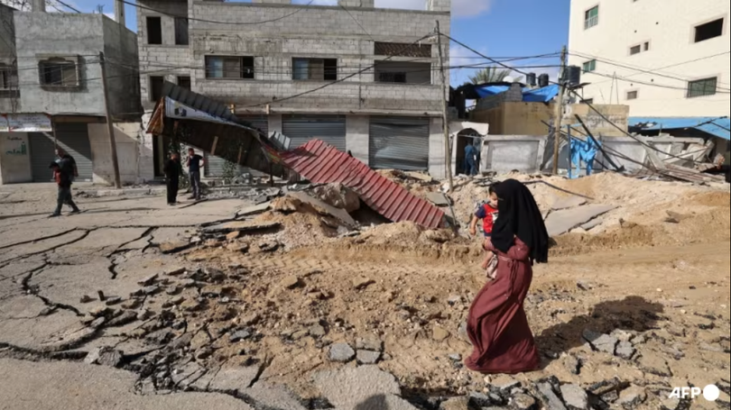 Một người phụ nữ đi bộ qua một con đường bị phá hủy sau cuộc không kích của Israel tại Khan Younis ở phía nam Dải Gaza vào ngày 14/5. Ảnh: AFP.