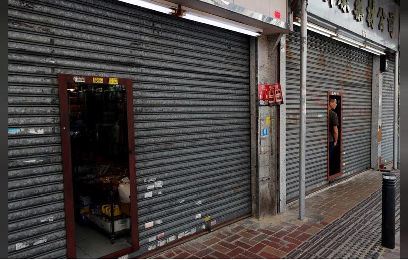 Chủ một cửa hiệu quan sát cuộc biểu tình qua cánh cửa đóng kín tại Sheung Shui (Ảnh: Reuters)