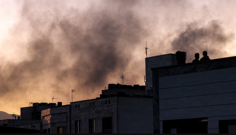 Người dân Iran đứng trên nóc tòa nhà giữa làn khói bốc lên nghi ngút sau cuộc không kích của Israel nhằm vào Tehran, thủ đô Iran, ngày 17/6. Ảnh: AFP.