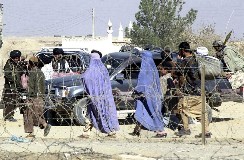Những người phụ nữ Afghanistan phải phủ Burqa kín mít đi ngang qua các tay súng Taliban, năm 2001 (Ảnh: AFP)