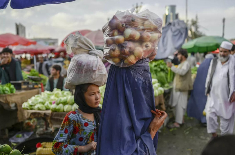 Một người phụ nữ mang burqa che kín mặt đội một túi hành tây trên đầu bên trong một khu chợ, ngày 22/9/2021 (Ảnh: AFP)