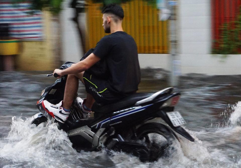 Một người nước ngoài cố gắng đưa chân lên cao cho khỏi ướt giày khi qua đường ngập sâu. Ảnh: LĐ