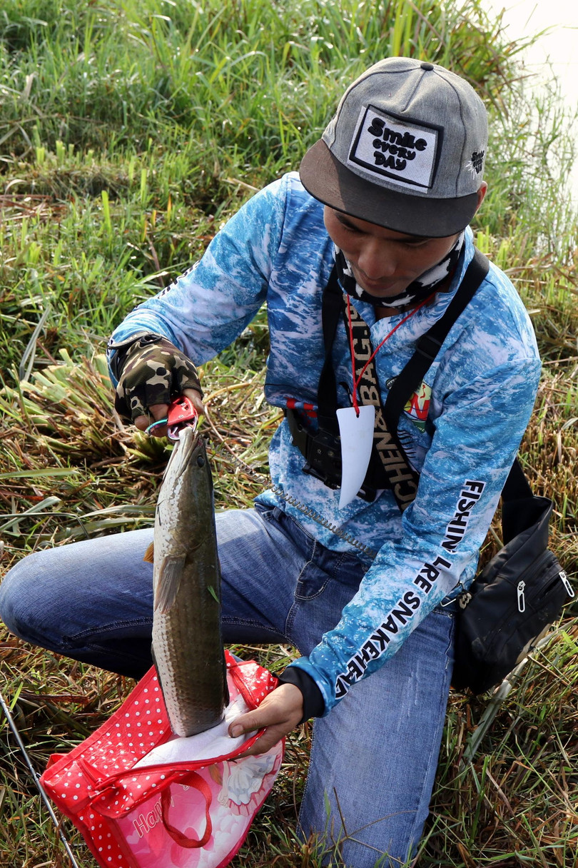 Trong lúc đó, ở một ao nhỏ xíu, thông với hồ, một cần thủ đã câu được con cá lóc to tướng, làm cho các trong tài và cả chàng phóng viên ảnh, ngẩn ngơ.