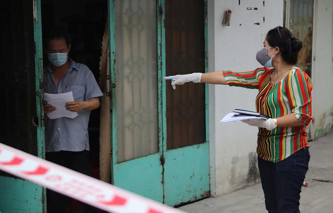Nhân viên trung tâm y tế quận 12 đến từng hộ dân trong khu phong tỏa ở phường Thạnh Lộc, quận 12, để đưa giấy khai báo y tế, sáng 8/2. Ảnh: Đình Văn.
