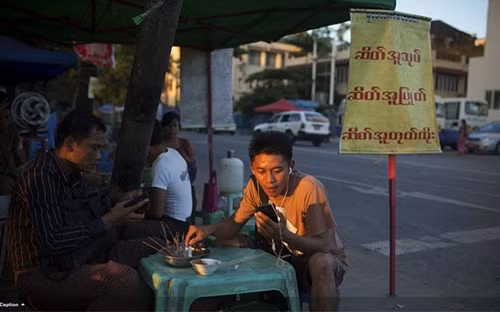 Sóng Viettel sắp chính thức phủ lên đất Myanmar. Trong ảnh là một người đàn ông Myanmar sử dụng điện thoại di động khi đang ngồi quán vỉa hè ở Yangon - Ảnh: Bloomberg.