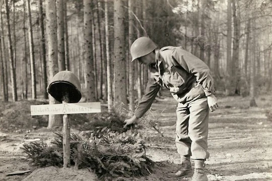 Một lính Mỹ đặt các cành thông lên mộ của lính Mỹ vô danh, bị quân Đức chôn trước khi rút lui.