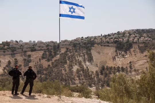 Lá cờ Israel tung bay, một phần của khu định cư Maale Adumim của Israel có thể được nhìn thấy ở phía sau, tại khu Bờ Tây do Israel chiếm đóng, ngày 14/8. Ảnh: Reuters.