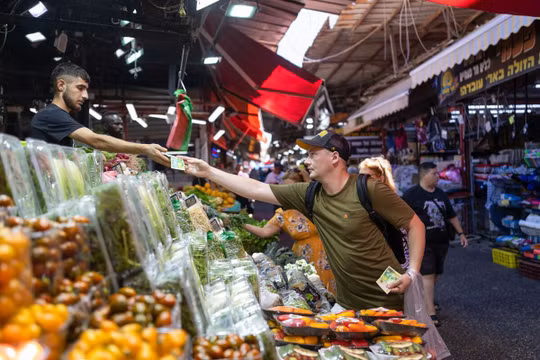 Một khách hàng mua nông sản tại một quầy hàng ở Tel Aviv, Israel (Ảnh: Bloomberg)