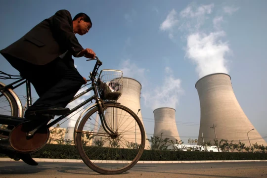 Một người đàn ông đạp xe qua ống khói của một nhà máy điện nằm ở ngoại ô Bắc Kinh vào ngày 29/10/2009. Ảnh: Reuters.