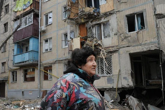 Một người phụ nữ đi qua tòa nhà bị hư hại do pháo kích ở Kharkiv, Ukraine (Ảnh: AP)