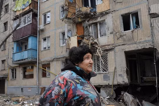 Một người phụ nữ đi qua tòa nhà bị hư hại do pháo kích ở Kharkiv, Ukraine (Ảnh: AP)