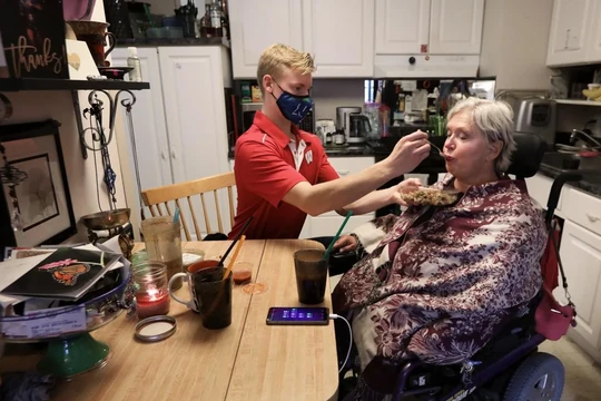 Nhân viên chăm sóc Andrew Wolfram giúp bà Karen Foxgiver ăn trưa bên trong căn hộ của bà (Ảnh: Madison)