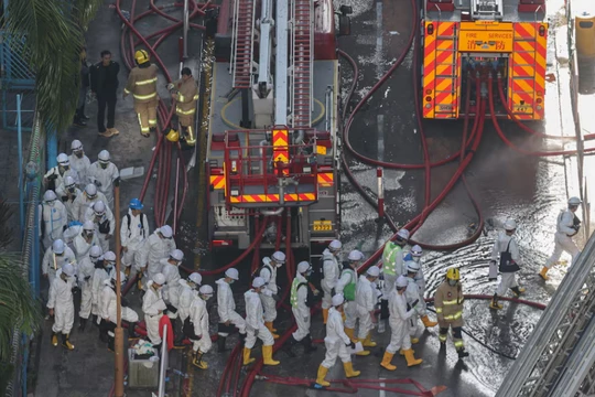 Cảnh sát mặc đồ bảo hộ đi bộ gần hiện trường vụ cháy chung cư tại khu nhà ở Wang Fuk Court sau vụ hỏa hoạn chết người ở Tai Po, Hong Kong, Trung Quốc, ngày 29/11. Ảnh: Reuters.