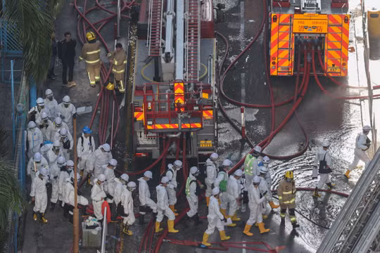 Cảnh sát mặc đồ bảo hộ đi bộ gần hiện trường vụ cháy chung cư tại khu nhà ở Wang Fuk Court sau vụ hỏa hoạn chết người ở Tai Po, Hong Kong, Trung Quốc, ngày 29/11. Ảnh: Reuters.