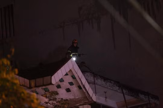 Lính cứu hỏa trèo lên nóc nhà kế bên để cứu hộ cứu nạn.