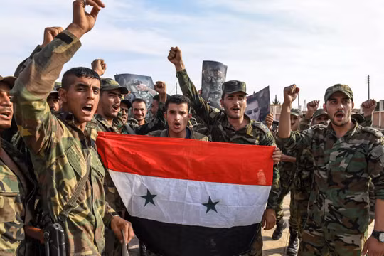 Quân đội chính phủ Syria giơ cao quốc kỳ và ảnh Tổng thống Assad tại ngoại ô thành phố Manbij hôm 15/10 (Ảnh: Newsweek)