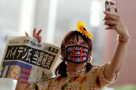 Một phụ nữ Nhật Bản chụp ảnh selfie với tờ báo đưa tin chiến thắng của Biden. (Ảnh: The Guardian)