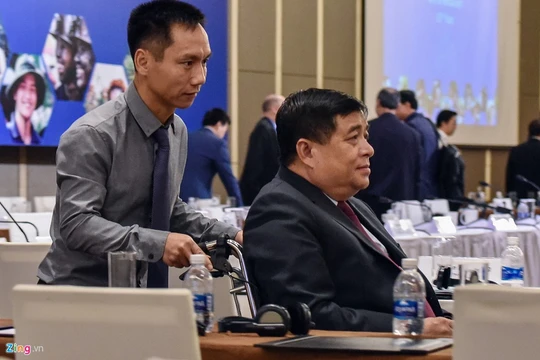 Bộ trưởng Nguyễn Chí Dũng phải ngồi xe lăn và nhờ người hỗ trợ khi đến dự diễn đàn. Ảnh: Việt Linh.