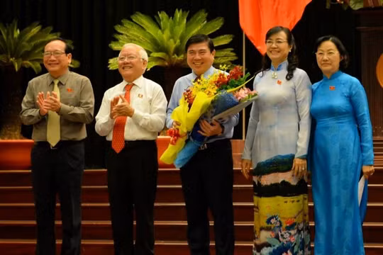 Chủ tịch UBND TP.HCM Nguyễn Thành Phong (giữa) nhận hoa chúc mừng từ ông Lê Hoàng Quân và bà Nguyễn Thị Quyết Tâm - Ảnh: Diệp Đức Minh