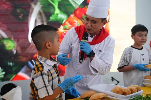 Chef tận tình hướng dẫn bé làm bánh mỳ. (Ảnh: VNA).