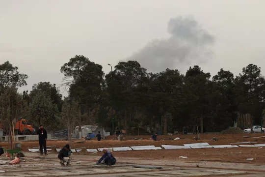 Người dân đang làm việc trong quá trình mở rộng nghĩa trang, trong khi khói bốc lên sau các cuộc không kích phía sau nghĩa trang Behesht-e Zahra ở Tehran, Iran ngày 16/3. Ảnh: Reuters.