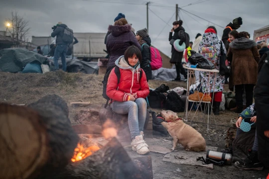 Một người phụ nữ và thú cưng của mình đang cố gắng sưởi ấm bên cạnh ngọn lửa. Ảnh: Guardian.