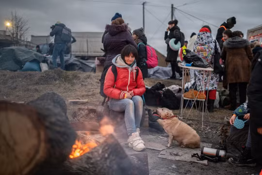 Một người phụ nữ và thú cưng của mình đang cố gắng sưởi ấm bên cạnh ngọn lửa. Ảnh: Guardian.