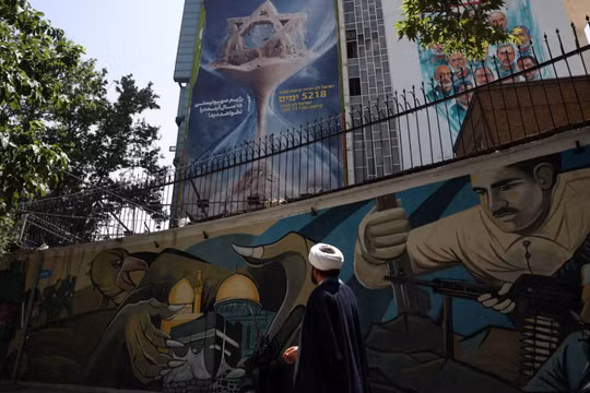 Một giáo sĩ Iran đi bộ bên cạnh một bảng quảng cáo chống Israel trên một tòa nhà ở Tehran, Iran, ngày 9/6. Ảnh: Ảnh: Reuters.