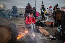 Một người phụ nữ và thú cưng của mình đang cố gắng sưởi ấm bên cạnh ngọn lửa. Ảnh: Guardian.