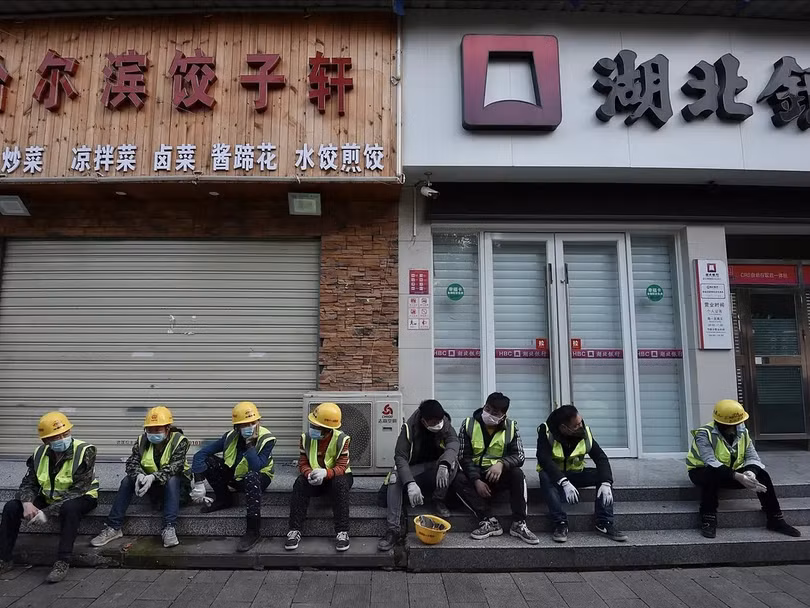 Công nhân ngồi bên ngoài một nhà hàng đã đóng cửa ở Vũ Hán, Trung Quốc ngày 23/2. Ảnh: AP