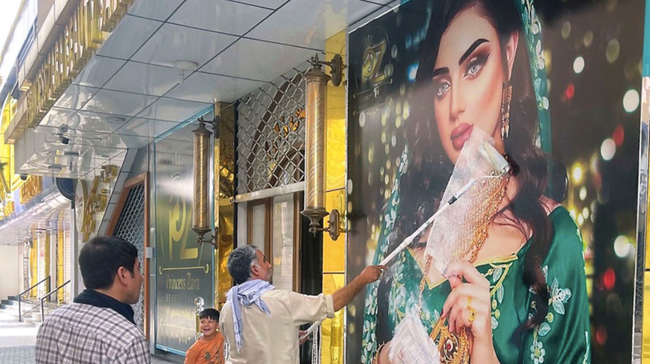 Một công nhân đang sử dụng sơn trắng để che hình ảnh quảng cáo váy cưới trước một cửa tiệm, theo chỉ thị của Taliban Một công nhân đang sử dụng sơn trắng để che hình ảnh quảng cáo váy cưới trước một cửa tiệm, theo chỉ thị của Taliban