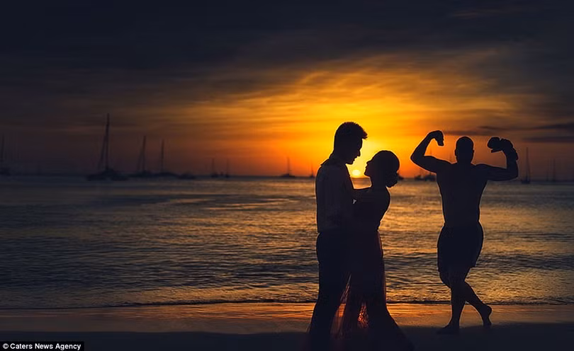 Vào chiều hoàng hôn lãng mạn, biển lặng yên không gợn sóng, cặp uyên ương nhìn nhau say đắm bên cạnh một người đàn ông đang... khoe cơ bắp.