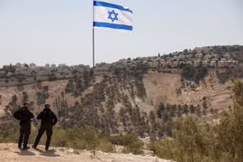 Lá cờ Israel tung bay, một phần của khu định cư Maale Adumim của Israel có thể được nhìn thấy ở phía sau, tại khu Bờ Tây do Israel chiếm đóng, ngày 14/8. Ảnh: Reuters.