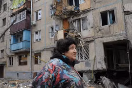 Một người phụ nữ đi qua tòa nhà bị hư hại do pháo kích ở Kharkiv, Ukraine (Ảnh: AP)