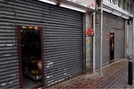 Chủ một cửa hiệu quan sát cuộc biểu tình qua cánh cửa đóng kín tại Sheung Shui (Ảnh: Reuters)