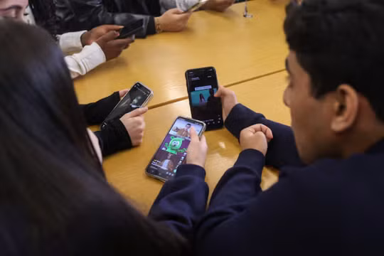 Các học sinh tại Wimbledon đang xem điện thoại di động trong một cuộc phỏng vấn với Reuters về quan điểm của họ về lệnh cấm mạng xã hội. Ảnh: Reuters.