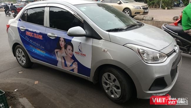 Các taxi công nghệ đều không niêm yết số điện thoại của đơn vị kinh doanh ở hai bên thân xe hoặc hai bên cánh cửa xe. Ảnh: Một xe tuân thủ việc dán logo Grab tại phía trên, bên trái của kính chắn gió nhưng không niêm yết thông tin hãng.