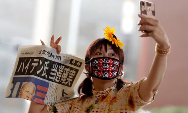 Một phụ nữ Nhật Bản chụp ảnh selfie với tờ báo đưa tin chiến thắng của Biden. (Ảnh: The Guardian)