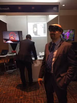 Ông Rafic, đeo cả kính cận và Hololen, đang nhìn thấy một con chuột đang chạy trong bánh xe quay màu đỏ vốn hoàn toàn vô hình nếu nhìn bằng mắt thường trong không gian thực của khách sạn Sheraton (hình ảnh này được hiển thị ra màn hình phía sau bên phải của ông)