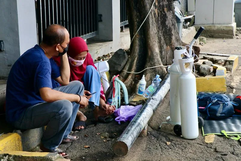 Bệnh nhân ngồi chờ giường bệnh ở bệnh viện tự mang theo bình oxy tới (Ảnh: Zaobao). Bệnh nhân ngồi chờ giường bệnh ở bệnh viện tự mang theo bình oxy tới (Ảnh: Zaobao).