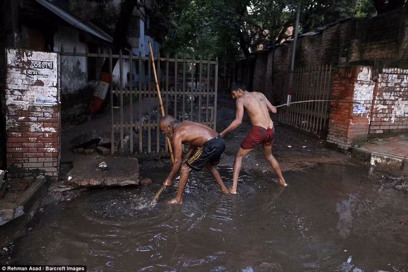Hai người đàn ông này cố gắng dùng gậy để khều rác lên khỏi ống cống, làm như vậy họ sẽ không phải ngụp lặn trong làn nước đen sì Hai người đàn ông này cố gắng dùng gậy để khều rác lên khỏi ống cống, làm như vậy họ sẽ không phải ngụp lặn trong làn nước đen sì