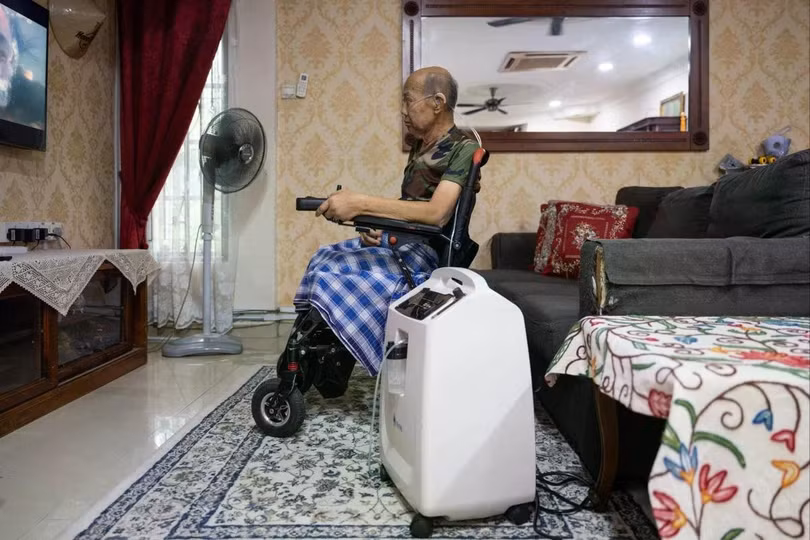 Ông Md Noor Bin Bujang xem truyền hình trong khi sử dụng máy tạo oxy tại nhà riêng ở Rawang, bang Selangor, Malaysia, hôm 16/10. Ảnh: AFP.