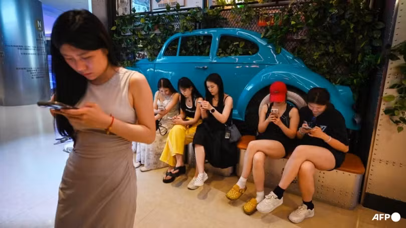 Người dân sử dụng điện thoại di động khi chờ chỗ trong một nhà hàng ở khu thương mại trung tâm Bắc Kinh ngày 11/7 (Ảnh: AFP)
